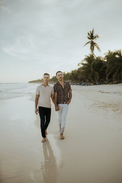 Dr. Michael and his husband Todd walk hand in hand along a tropical beach during the Golden Hour.
