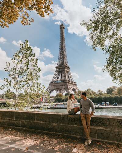 man and woman sitting on stone wall with eiffel tower in background