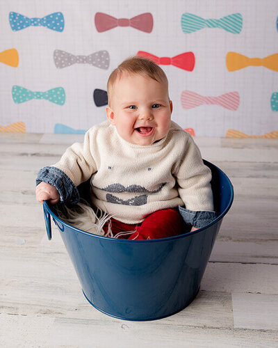 Happy baby sitting in a blue bucket with bow ties.