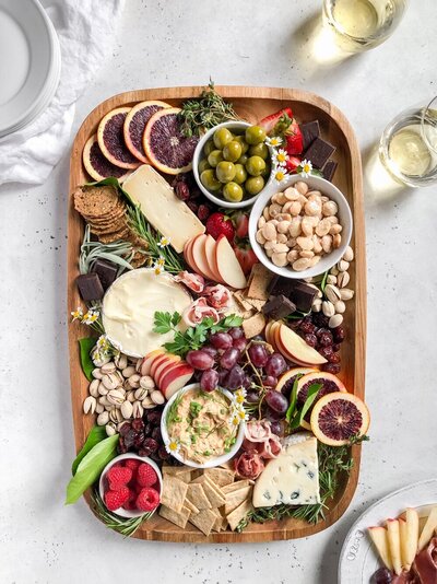 Large cheese board filled with an assortment of cheeses, bread and fresh fruit by Fed & Full Tables & Boards.