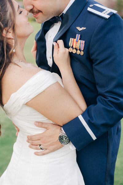 A bride and groom embracing on their wedding day, the groom in a military uniform with medals, captured by a luxury wedding photographer.