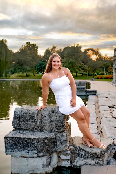 A gorgeous brunette girl is posing against a rock in Tower Grove Park for her senior portrait session.