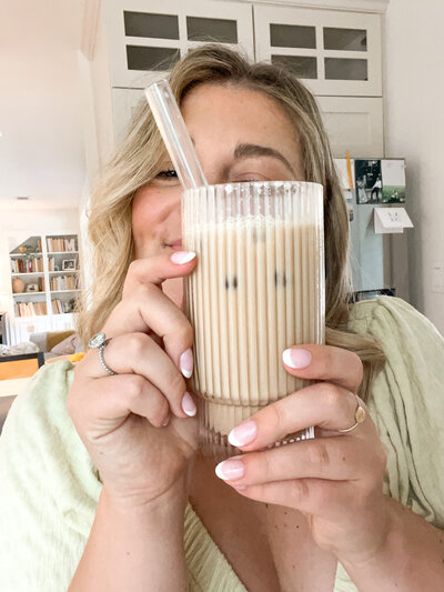Mollie Mason holding up a clear glass of iced coffee with a straw in front of her face