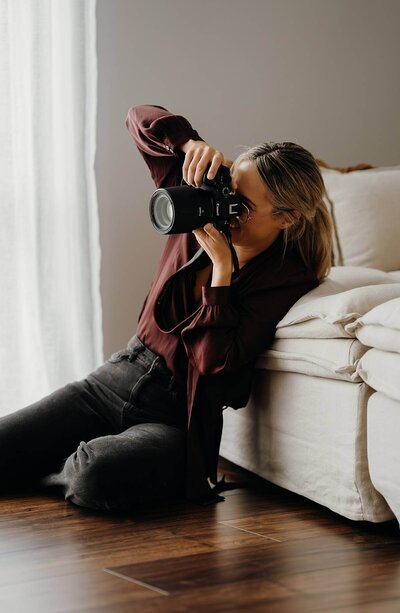 New plymouth photographer aimee kelly sitting on the ground in her studio taking a photograph of someone who is out of frame