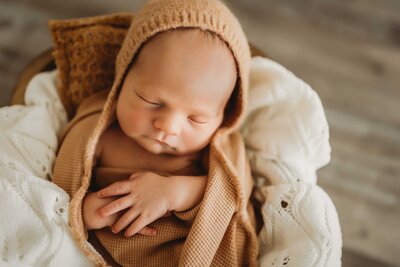 Newborn baby crossing his arms on top of his belly while he sleeps. The baby is wrapped in a blanket and looks peaceful and dreamy.