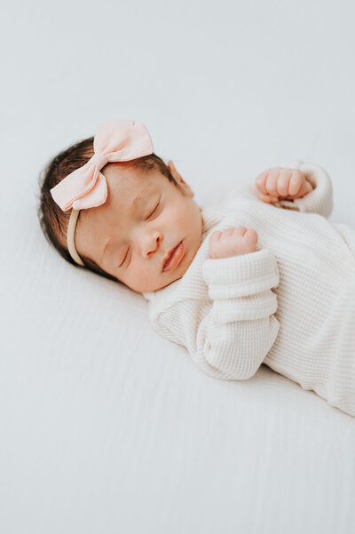 newborn baby girl with pink bow poses during photo session at Worth Capturing studio in Raleigh NC