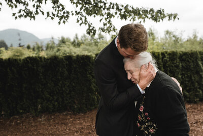 Emotional moment of groom hugging Oma at outdoor wedding.
