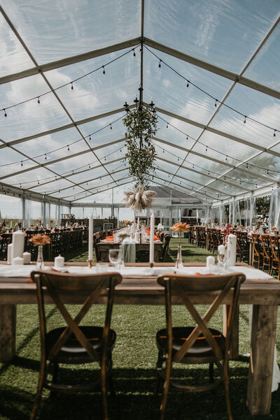 clear tent with hanging greenery, wood tables and candles