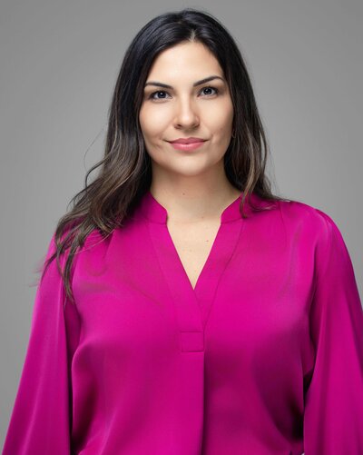 Professional headshot of Rocio with a confident smile, photographed on a soft gray background using flattering natural-style lighting by Liza Hondros Photography.