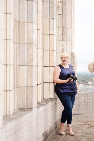 st-louis-newborn-photographer-holding-camera-smiling-with-blonde-hair-wearing-blue-sparkly-top