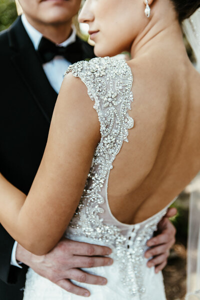 Bride and groom embracing with focus on the low-backed wedding dress