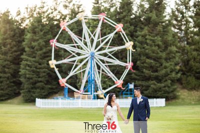 Newly married couple go for a walk holding hands in front of the Ferris Wheel at the Calamigos Ranch wedding venue in Malibu