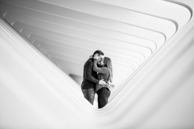 A couple kiss surrounded by modern architecture.