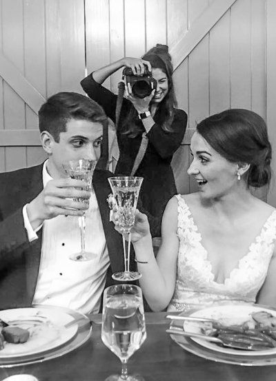 Behind the scenes image of a photographer photographing a newly married couple cheersing.