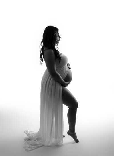 pregnant woman holding her belly wearing a white open belly dress