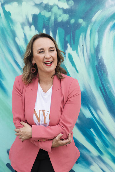 Woman with crossed arms laughing in front of blue wall