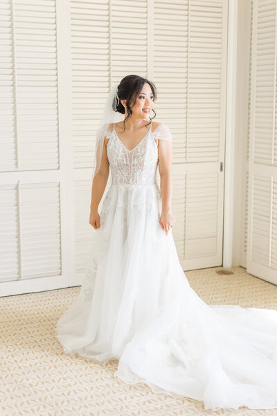 bride standing in her wedding dress looking over her left shoulder out the window