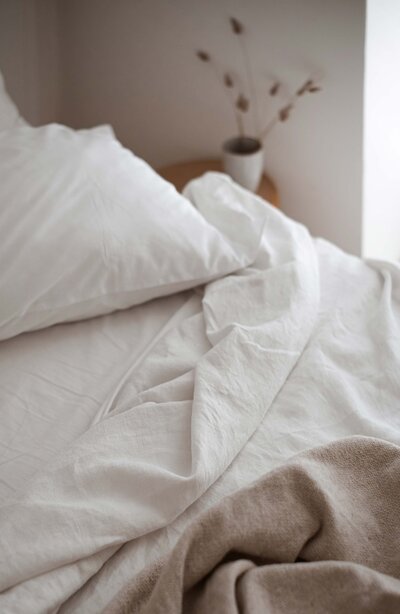 bed close-up, white pillow, messy white sheets, round wooden nightstand with mug