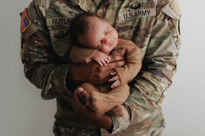 military dad holding newborn baby in brown outfit