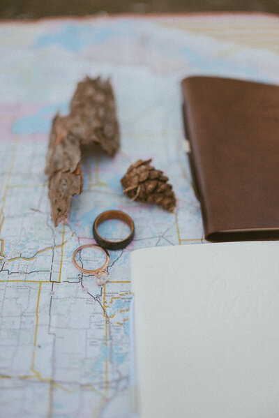 Wedding Rings on the map with vow books and pinecones