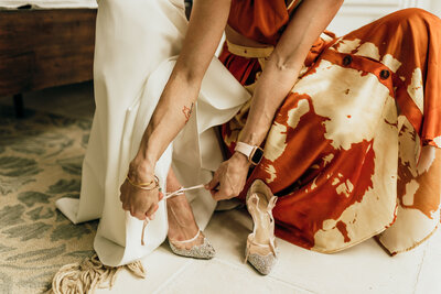 woman helps bride tie shoes