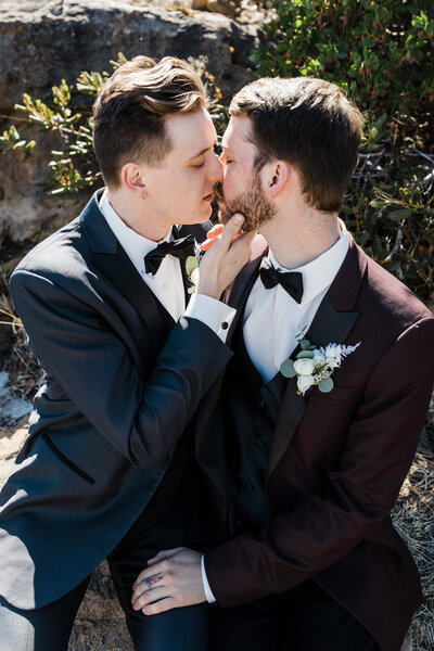 Two Grooms, one wearing a black suit and the other wearing a burgundy suit, share an intimate kiss at their Tetherow Resort Wedding in Bend, Oregon. | Erica Swantek Photography