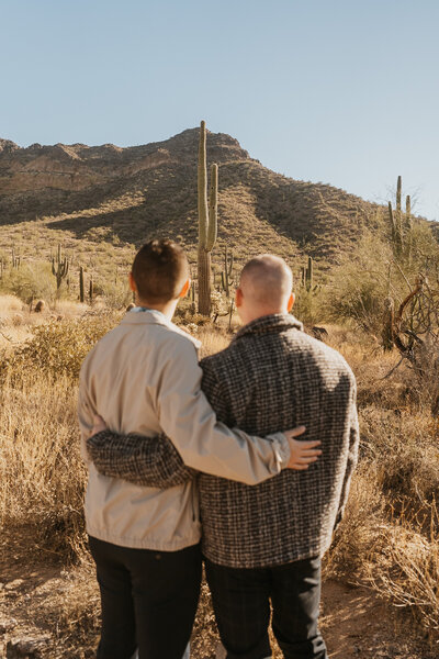 A couple with their arms around each other looking out over a desert landscape 