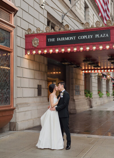 asain bride and groom kissing infront of the fairmont copley plaza hotel on a rainy summer day.