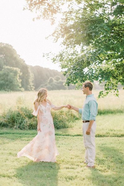 engaged couple twirl in a big open field at sunset