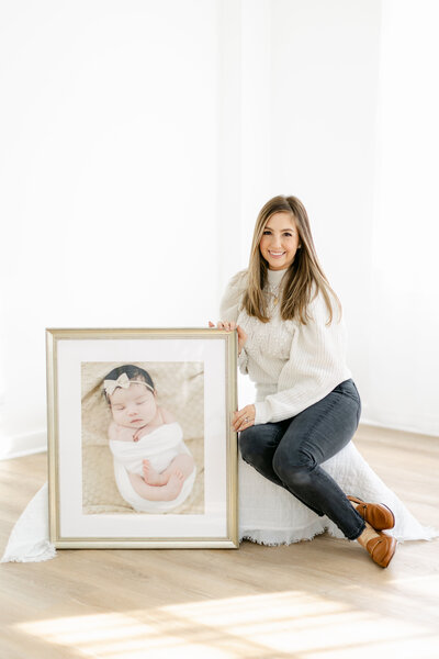 South Jersey Newborn Photographer Tara Federico holding a custom framed print of newborn baby girl