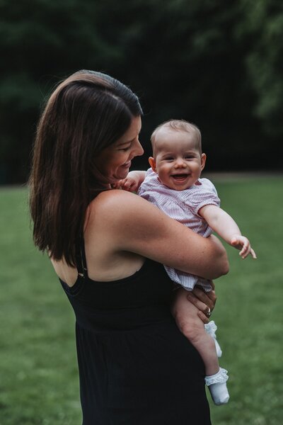 Mother in black dress holds her baby daughter who is smiling and laughing