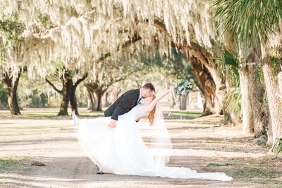 A newly married couple kissing under spanish moss trees during their winter wedding  in North Carolina, by JoLynn Photography