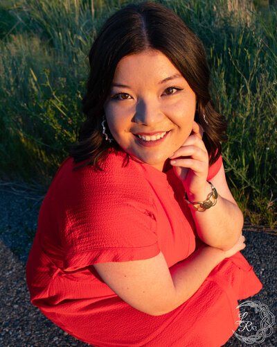 Photo of Ashlyn crouching in a red dress with her hand resting on her chin and smiling up at the camers