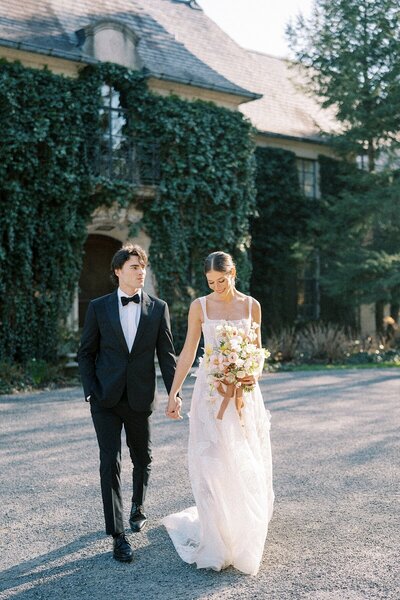Bride and Groom walking in front of Greencrest Manor in a Black tux and a Berta Wedding gown