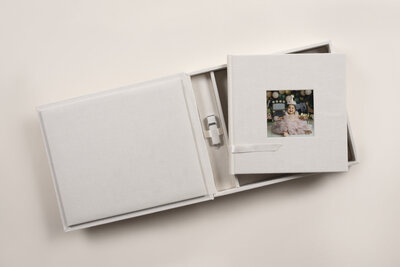 A photo album of a cake smash session sits on a box with a flash drive of the images inside