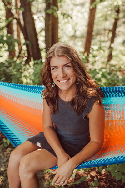 Woman sitting on a hammock in the woods smiling