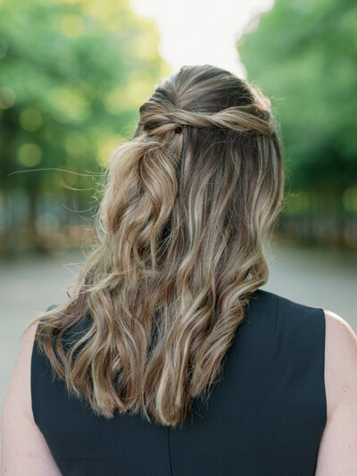 the back of a women's head  with her hair half up and a row of trees in the background