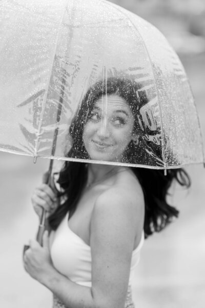 A black and white portrait of Nashville wedding photographer brooke elliott holding an umbrella over her face looking off to her right with rain droplets on the umbrella