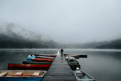 Moody mountain elopement, bride and groom standing on dock in Waterton Lakes National Park, captured by Love and be Loved Photography, authentic and adventurous wedding photographer and videographer in Lethbridge, Alberta. Featured on the Bronte Bride Vendor Guide.
