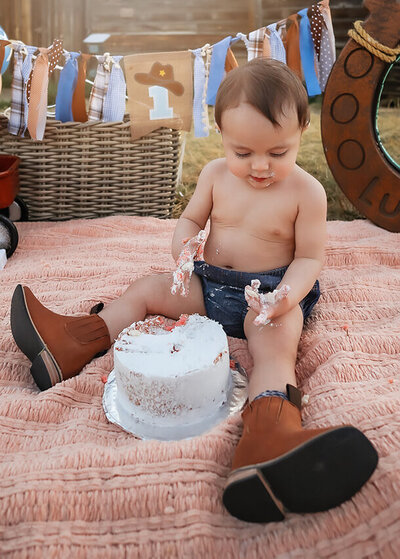 Cute kiddo playing with his cake at his outdoor first birthday session.