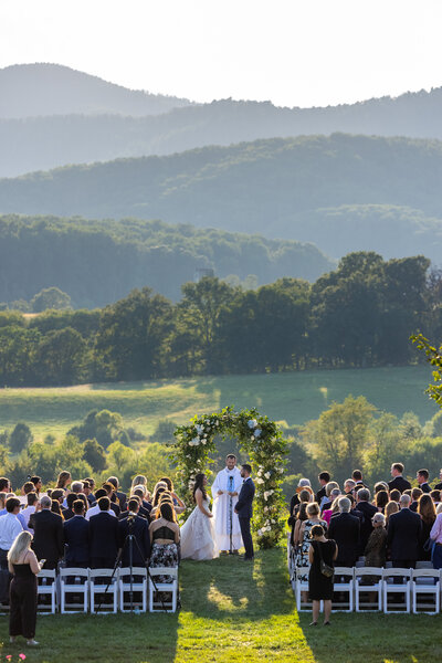 A bride and groom marry under a floral arch surrounded by guests at Pippin Hill Vineyards