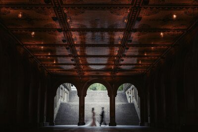 A blurred wedding couple walking at the base of a large staircase.