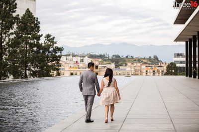Engaged couple walk hand in hand along side the reflection pool at the LA Department of Water and Power