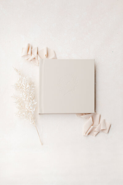 A cream photo album artfully displayed on ribbon with flowers next to it photographed by New Jersey Newborn Photographer Kate Voda Photography