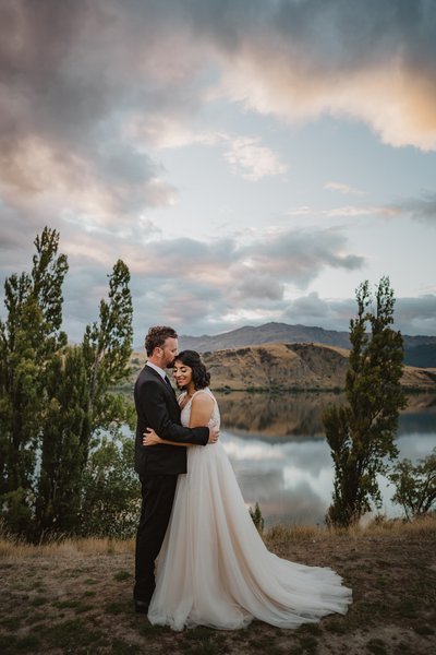 Bride and groom hugging at sunset infront of lake hayes