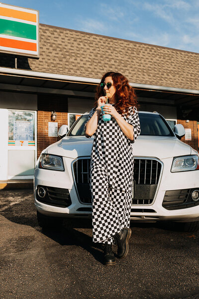 A person leaning on a car while sipping a slurpee.