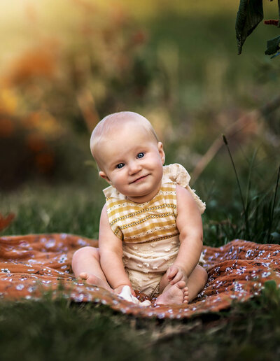 An adorable baby girl sitting on a blanket and smiling for an Asheville Photographer