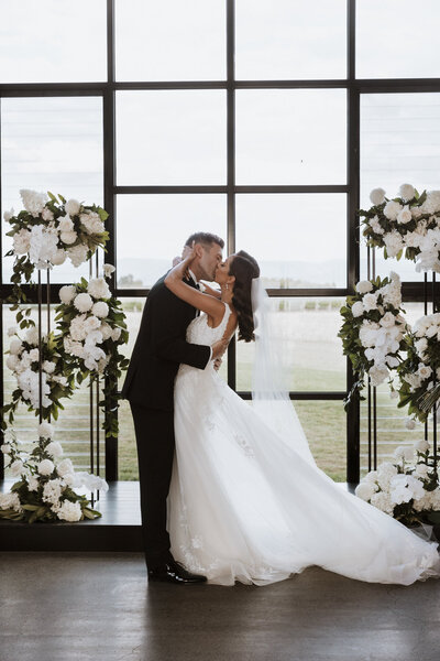 A couple kissing at the alter at Zonzo Estate with white floral pillars
