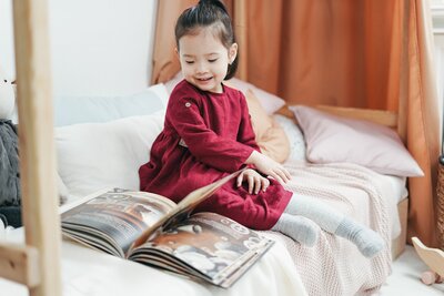 Asian girl elementary preschool student reading homeschool living book on bed