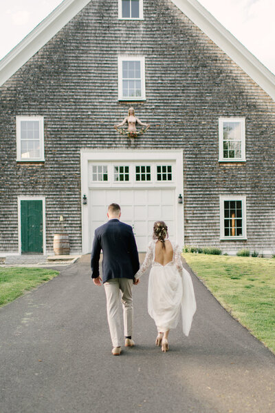 a bride and groom walk towards a barn